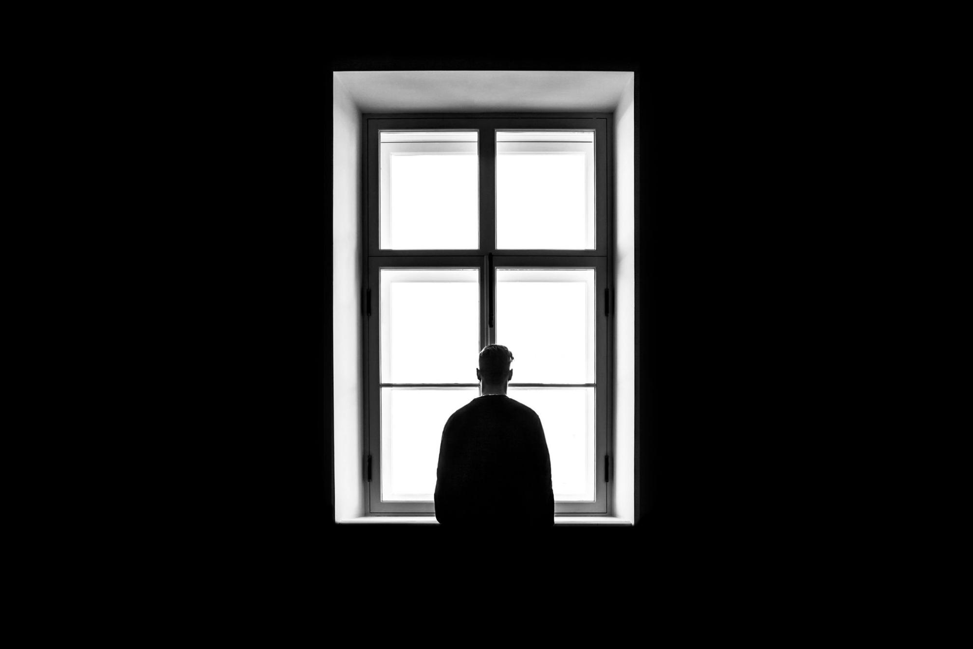 A man gazing out of a window, reflecting on unresolved trauma and processing trauma with the help of a trauma specialist.